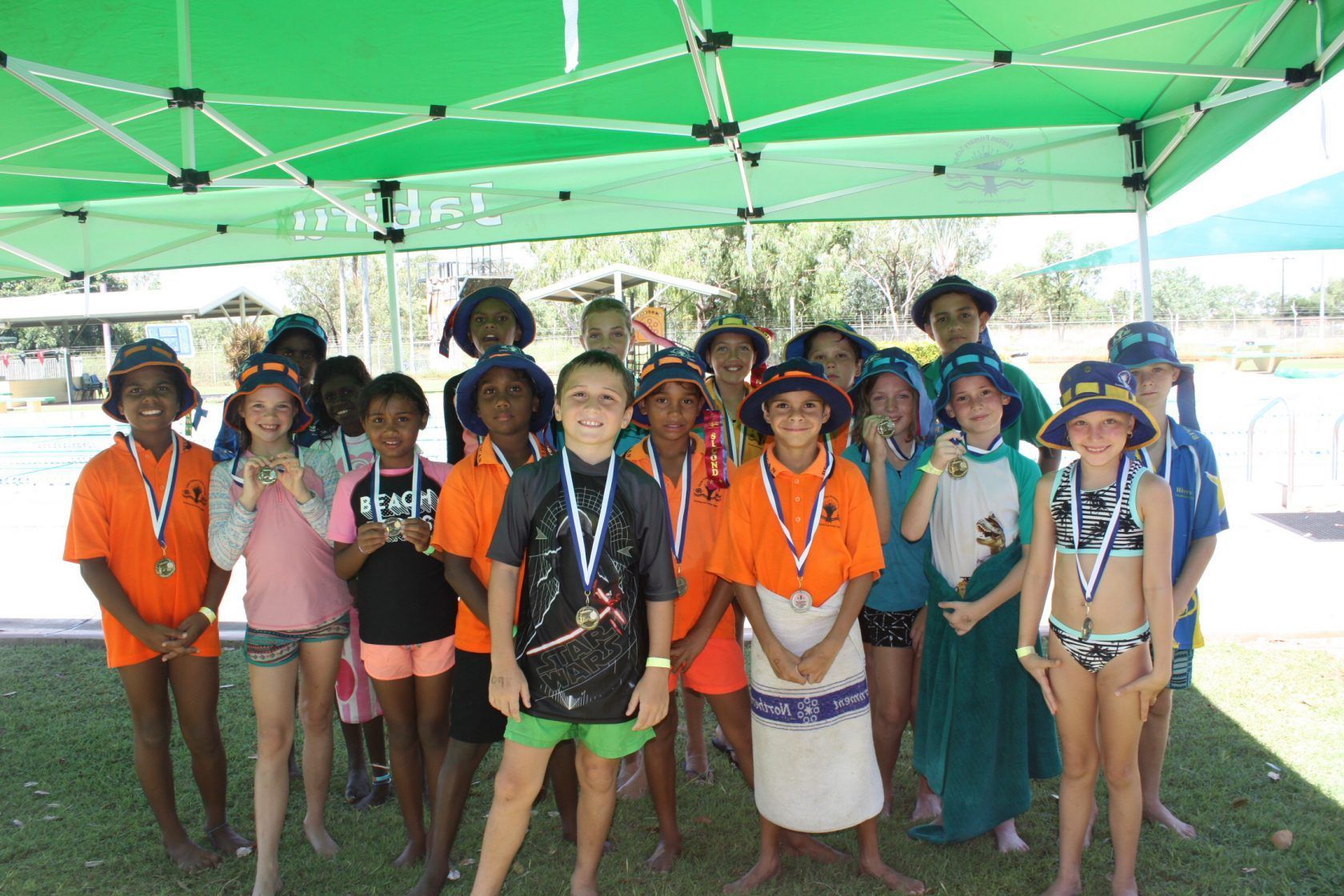 A group of children are posing for a picture under a green tent.