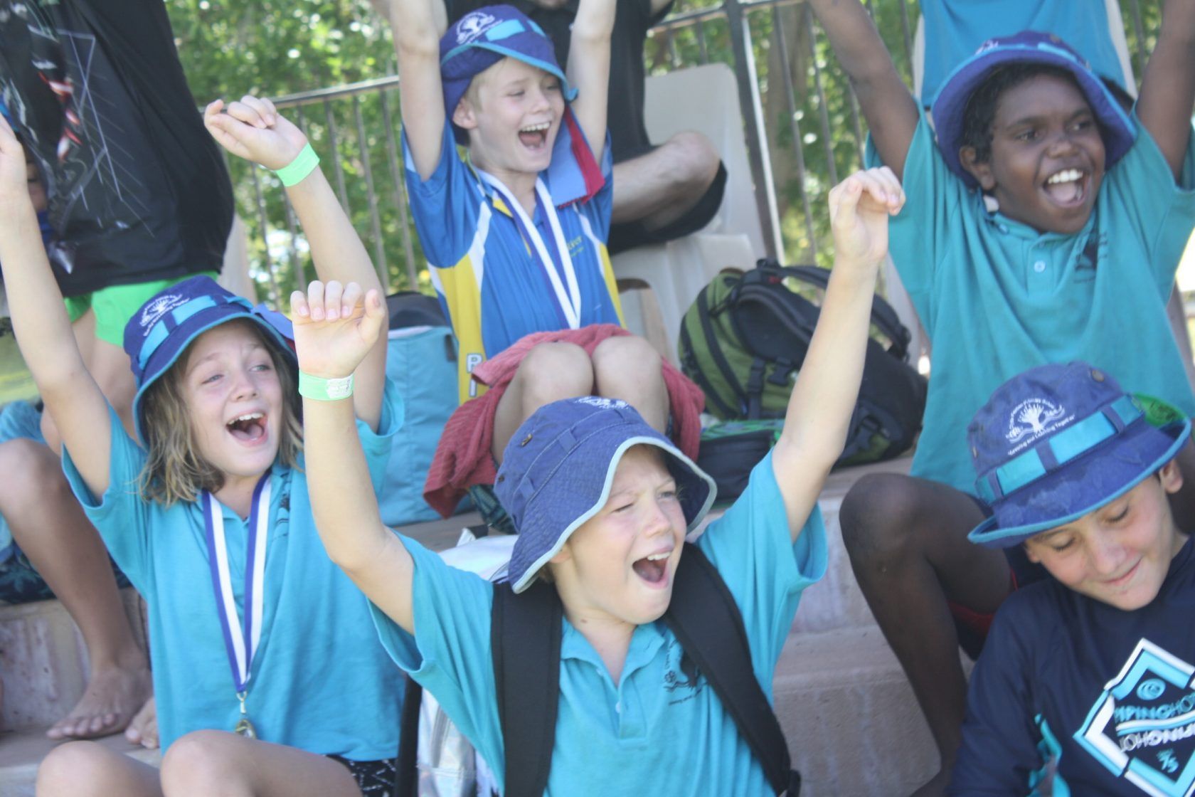 A group of children are sitting on a bench with their arms in the air.