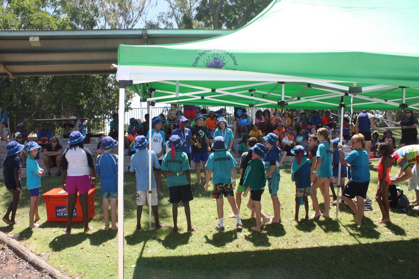 A group of children are standing under a green tent