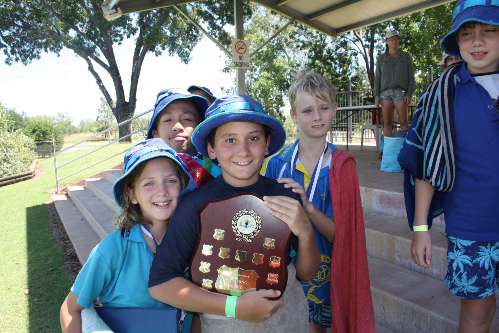 A group of children are posing for a picture and one of them is holding a plaque