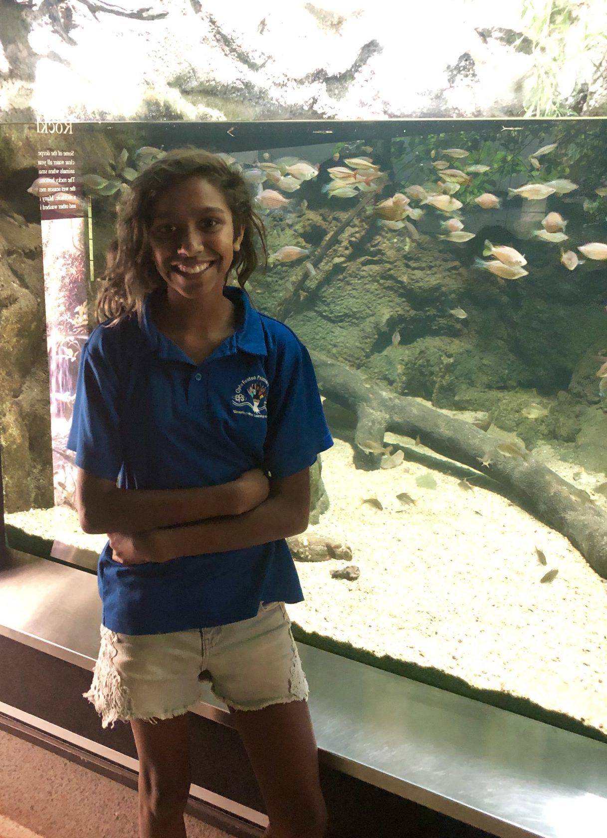 A young girl is standing in front of an aquarium with fish.