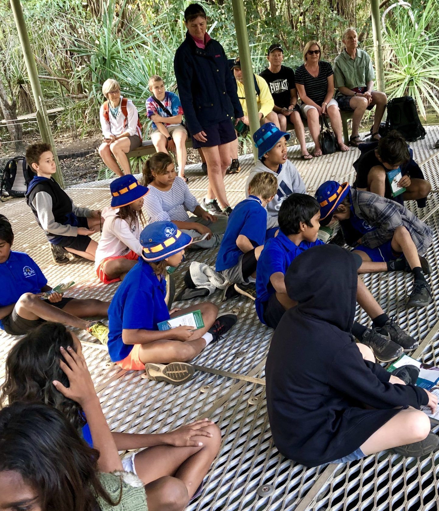 A group of children are sitting on a bench under a canopy.