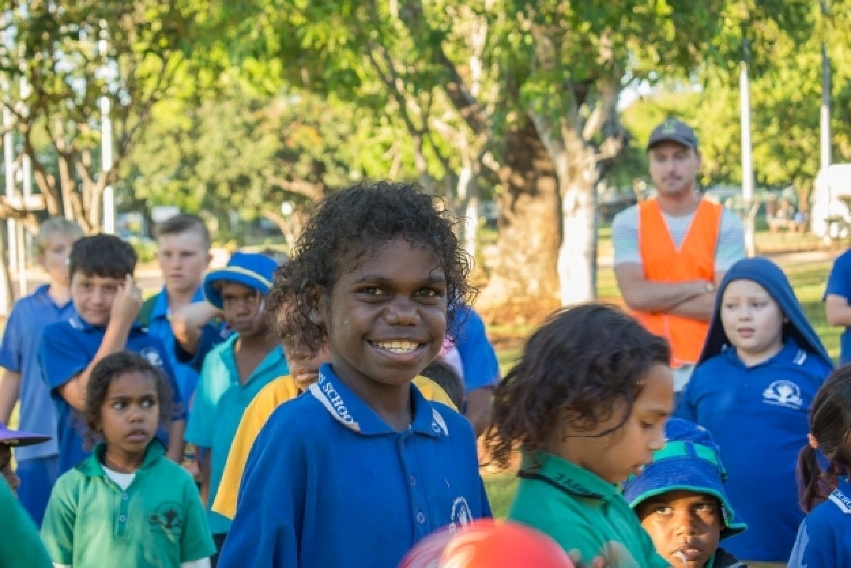 A group of children are standing in a park holding a red ball.