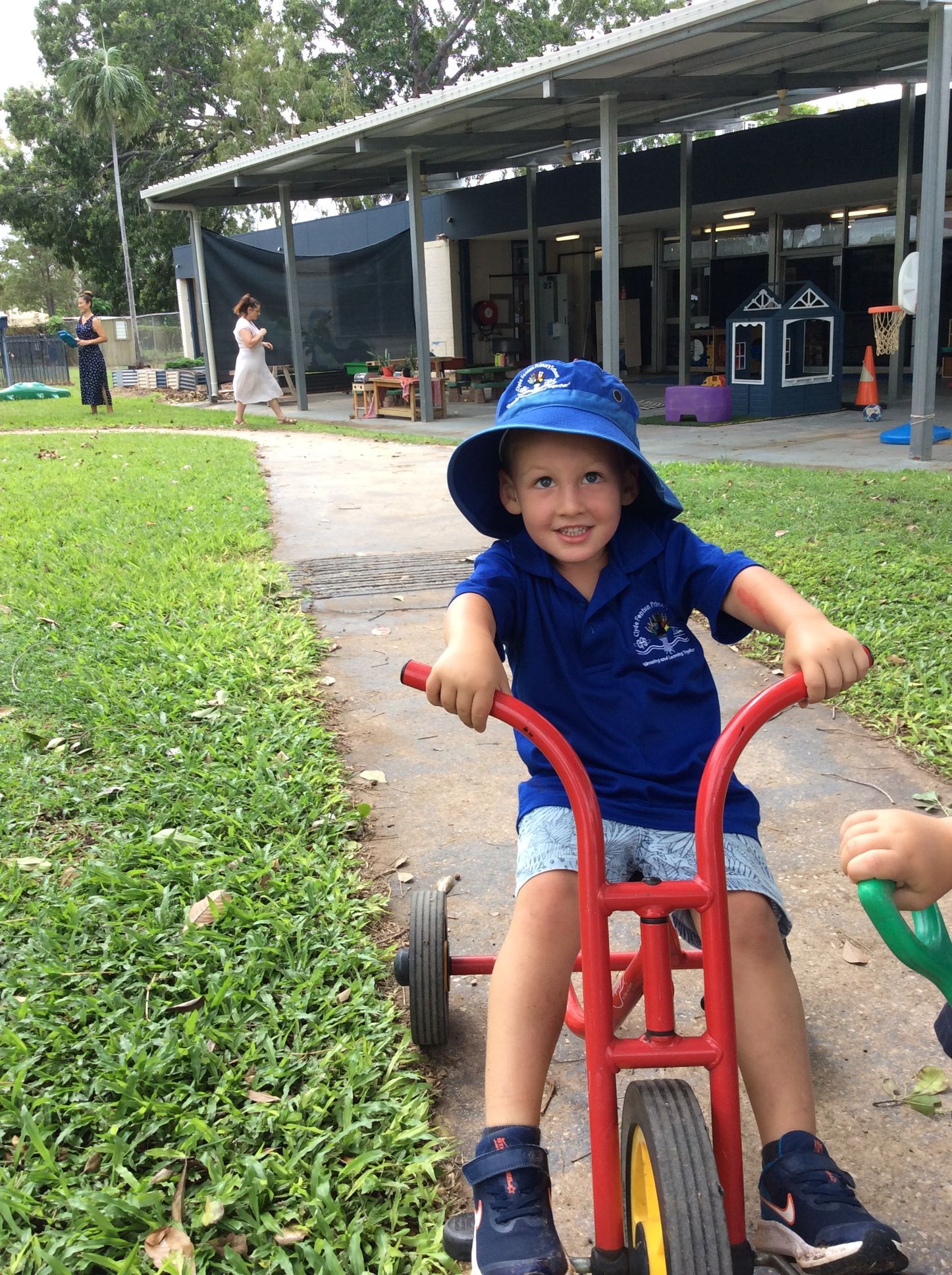 A young boy wearing a blue hat is riding a red tricycle