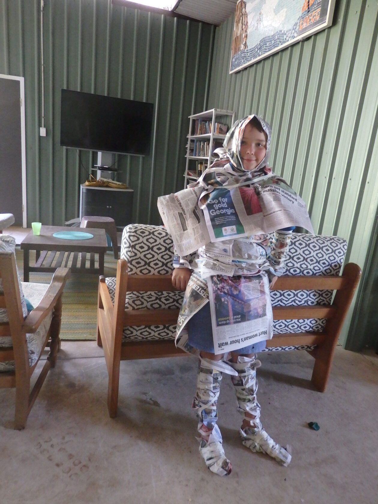 A person wrapped in newspaper is standing in a living room.
