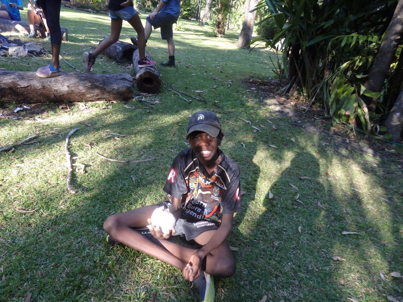 A young boy is sitting on the grass with his legs crossed.