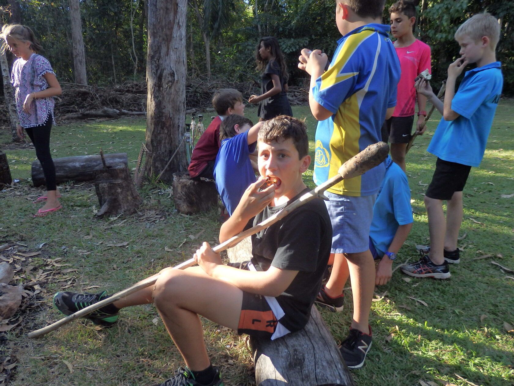 A boy is sitting on a log with a stick in his mouth