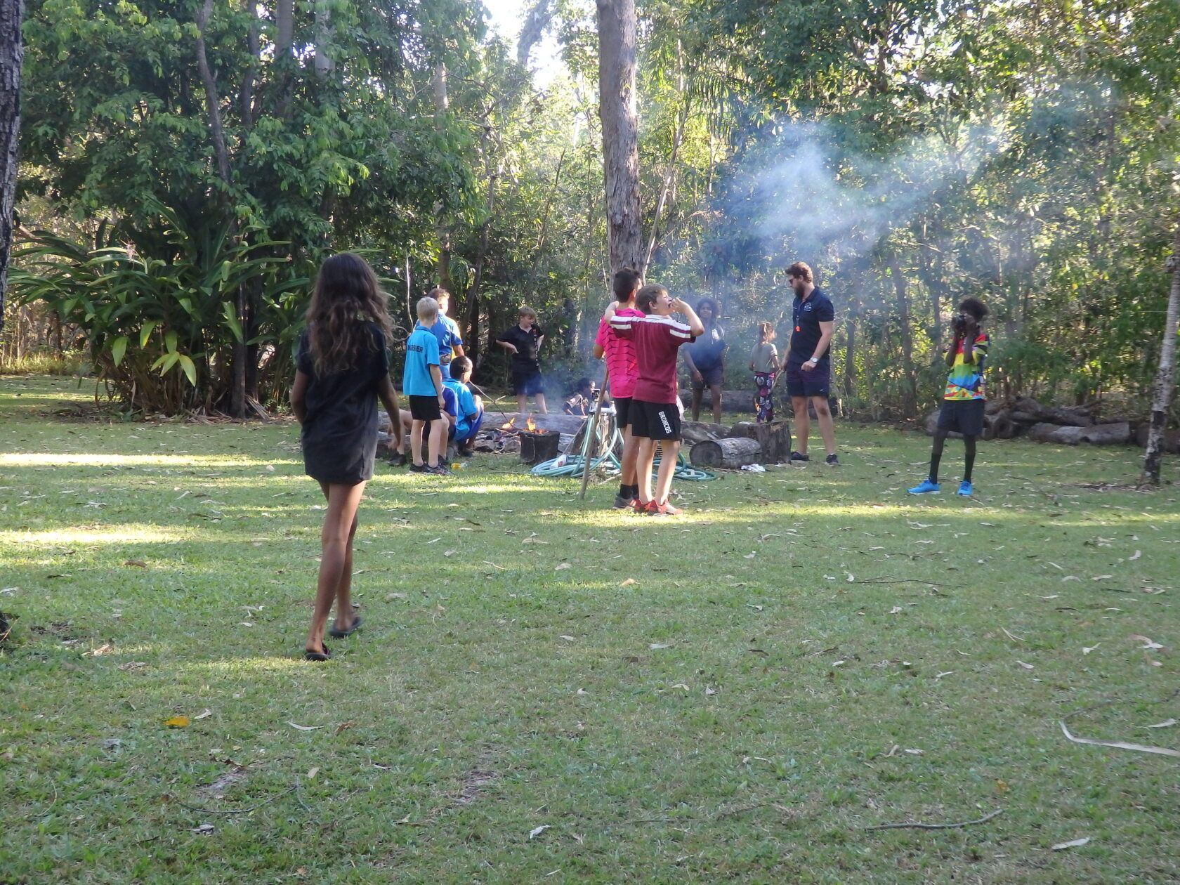 A group of people are standing around a campfire in a park.