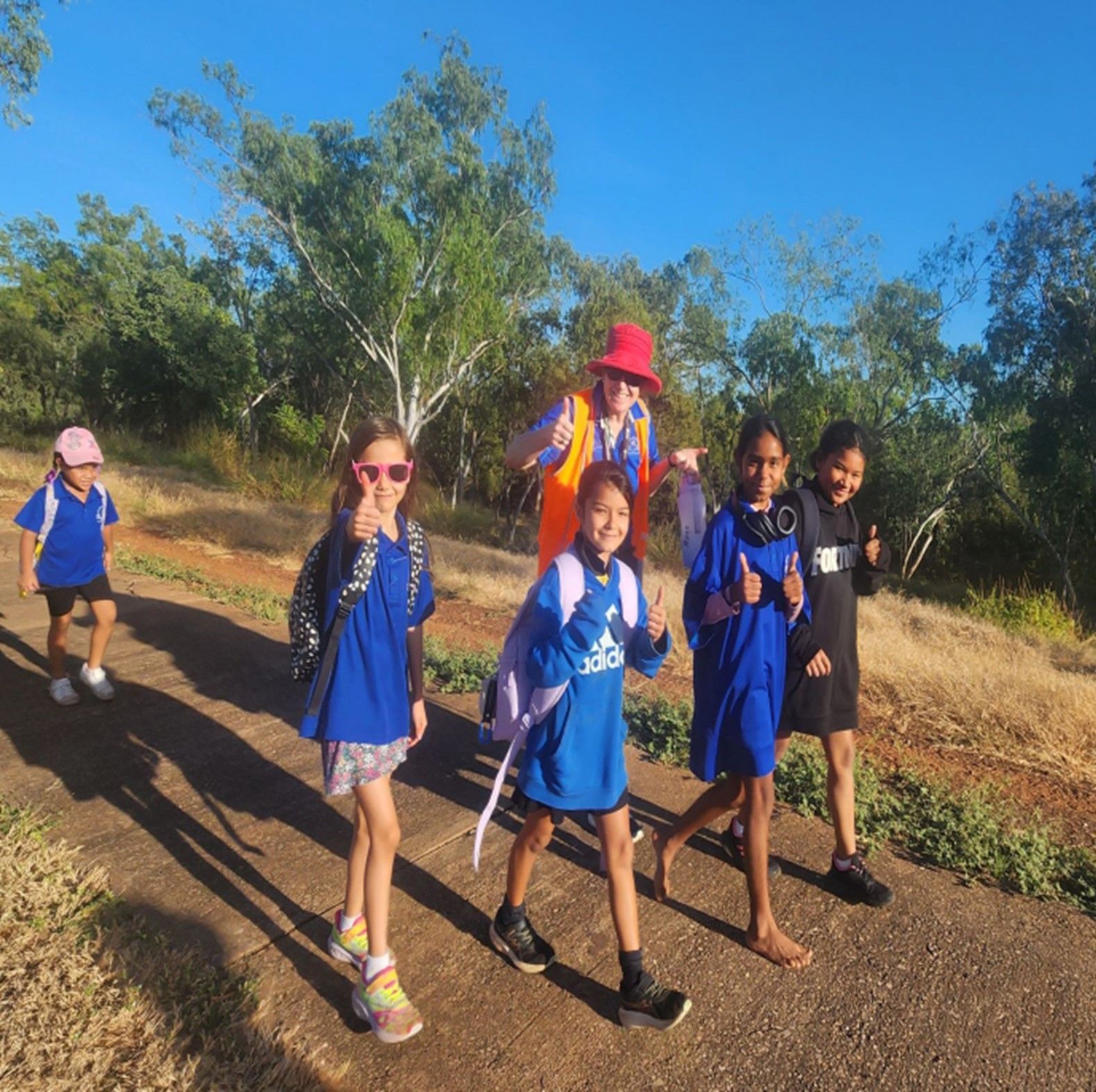 A group of children are walking down a road and one of them is wearing an adidas shirt