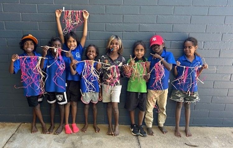 A group of children are standing in front of a brick wall holding yarn.