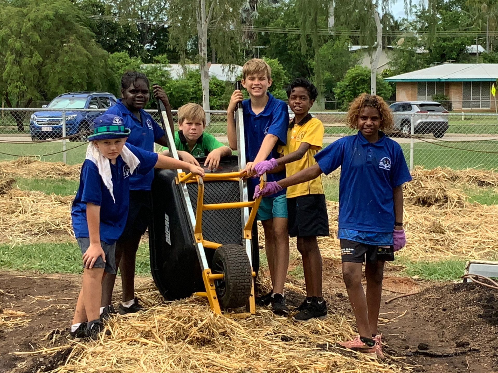 A group of children are standing around a wheelbarrow.