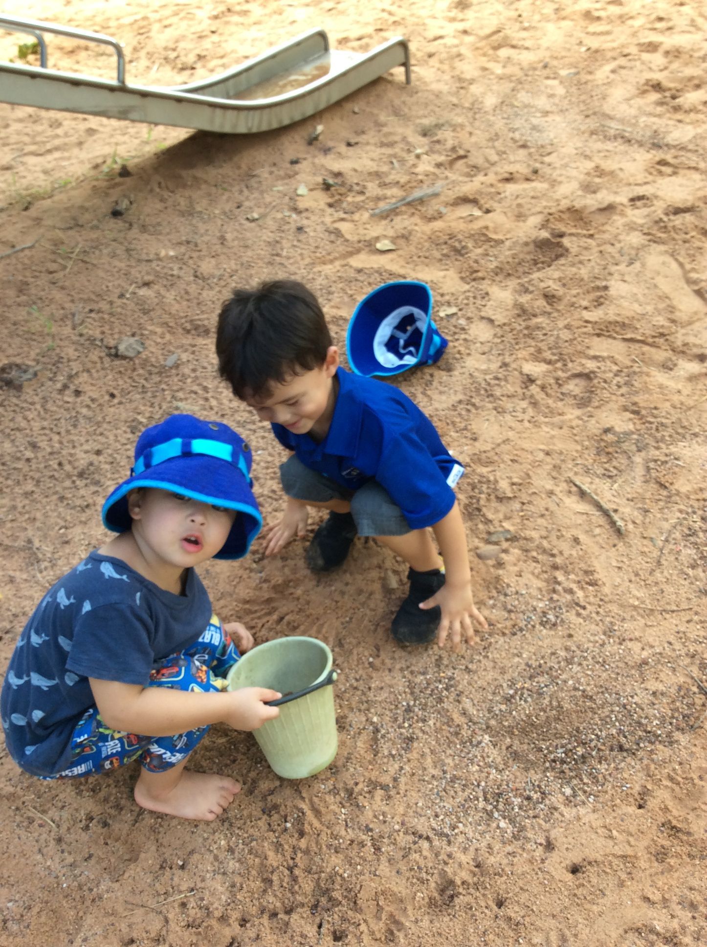 Two young boys are playing in the sand with buckets.