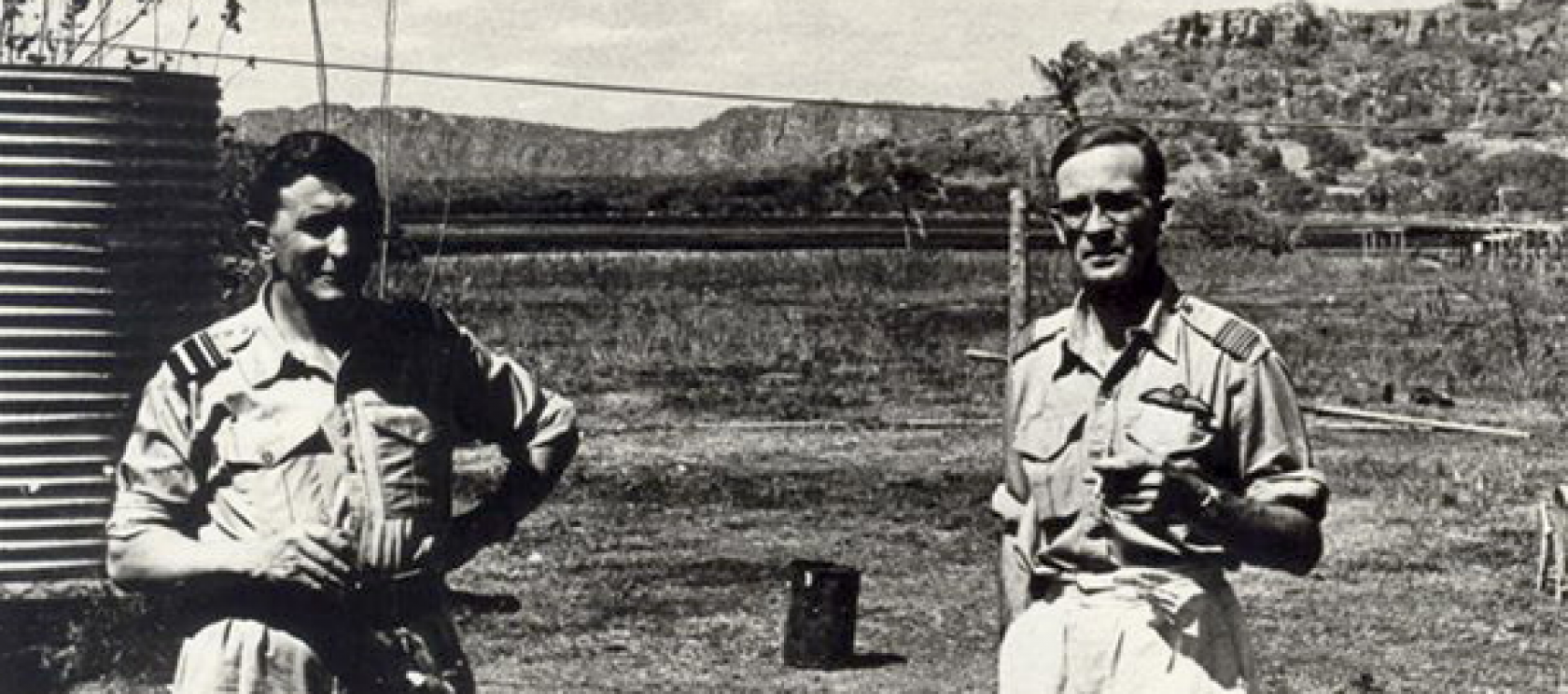 Two men in military uniforms are standing next to each other in a field.