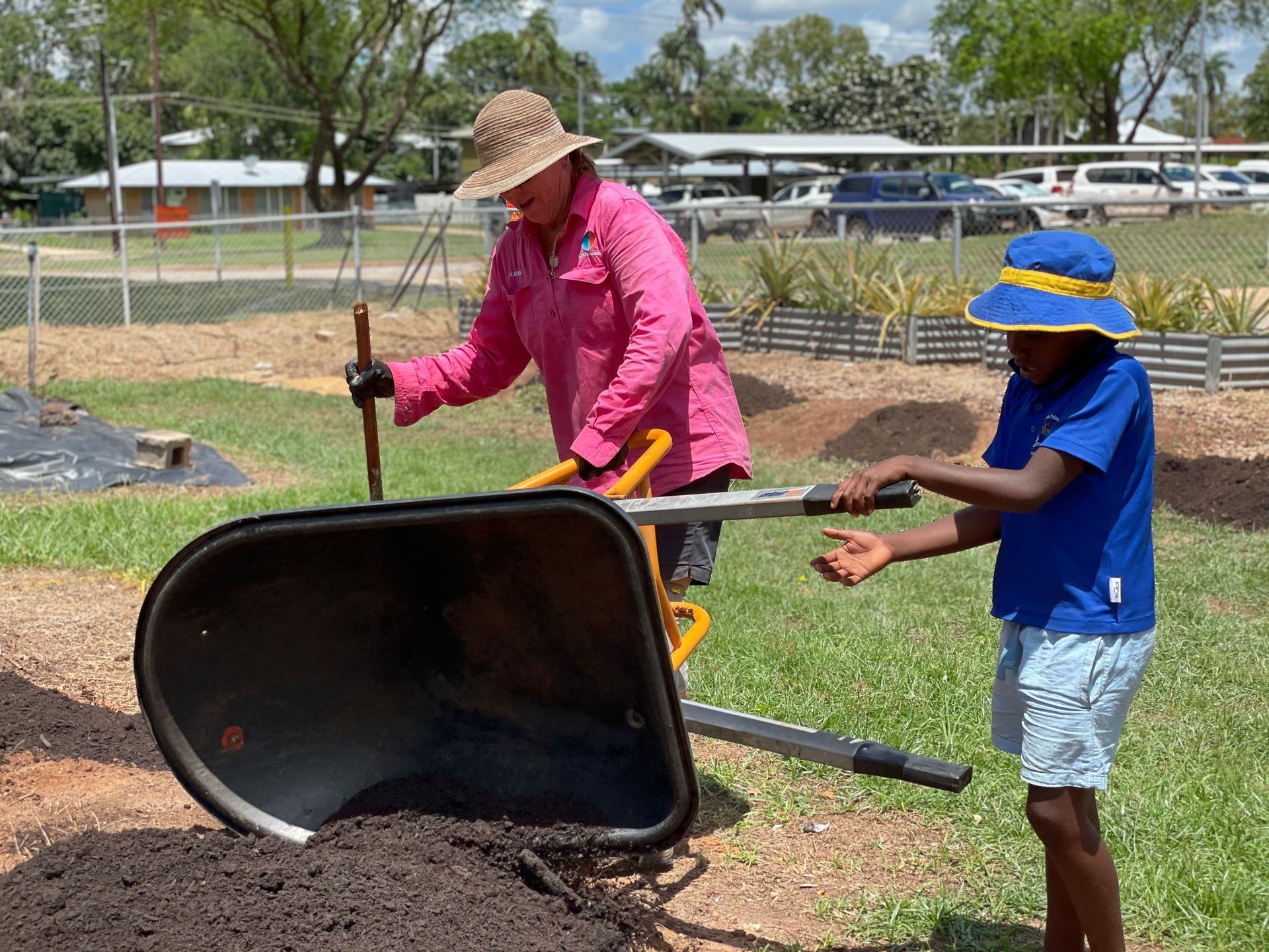 A woman and a child are pushing a wheelbarrow full of dirt.