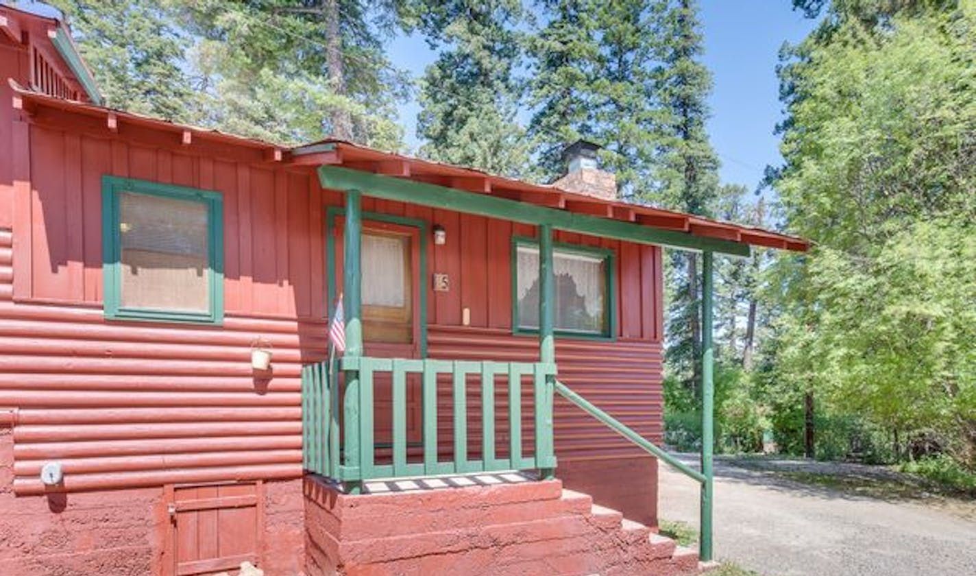 A red cabin with a green porch is surrounded by trees.