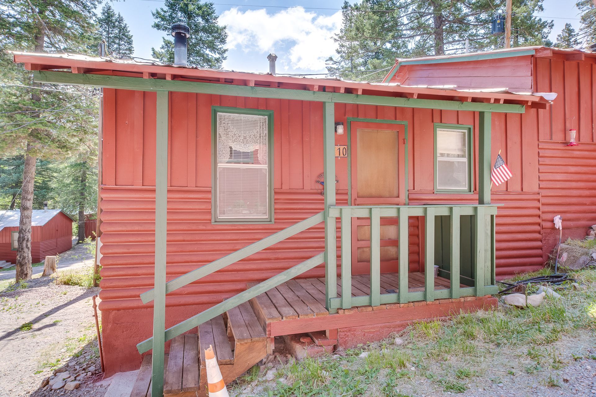 A red cabin with a green porch and stairs.