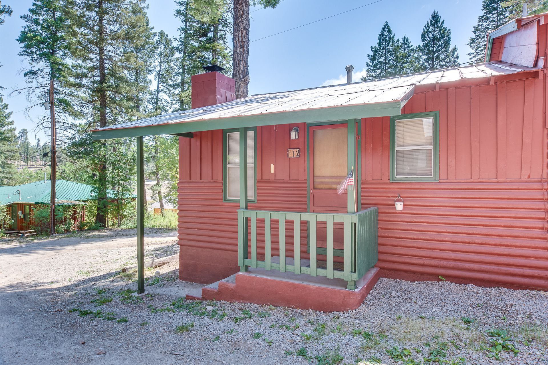 A red house with a green porch and trees in the background