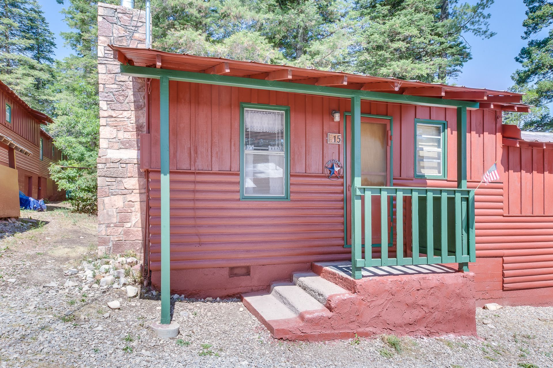 A small red cabin with a green porch and stairs.