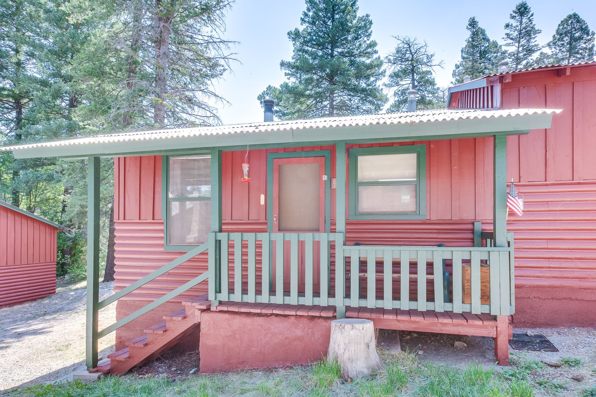 A small red cabin with a green porch and stairs.