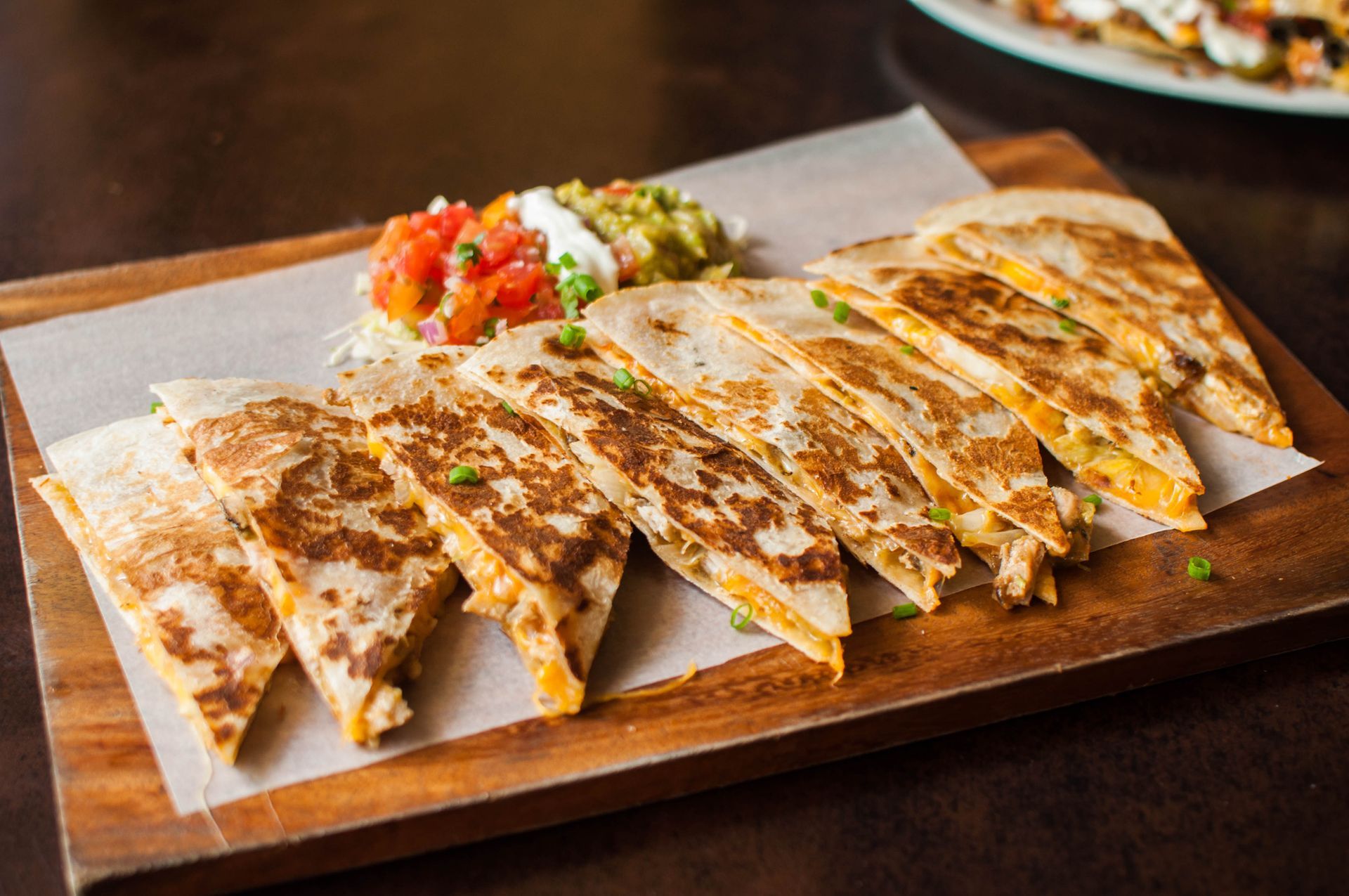 Quesadillas cut into triangles on a wooden board, with salsa, guacamole, and sour cream.