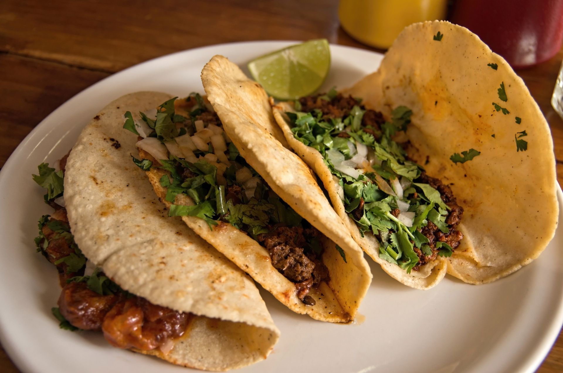 Three tacos on a white plate, filled with meat, cilantro, and onion, with a lime wedge. Three tacos on a white plate, filled with meat, cilantro, and onion, with a lime wedge.
