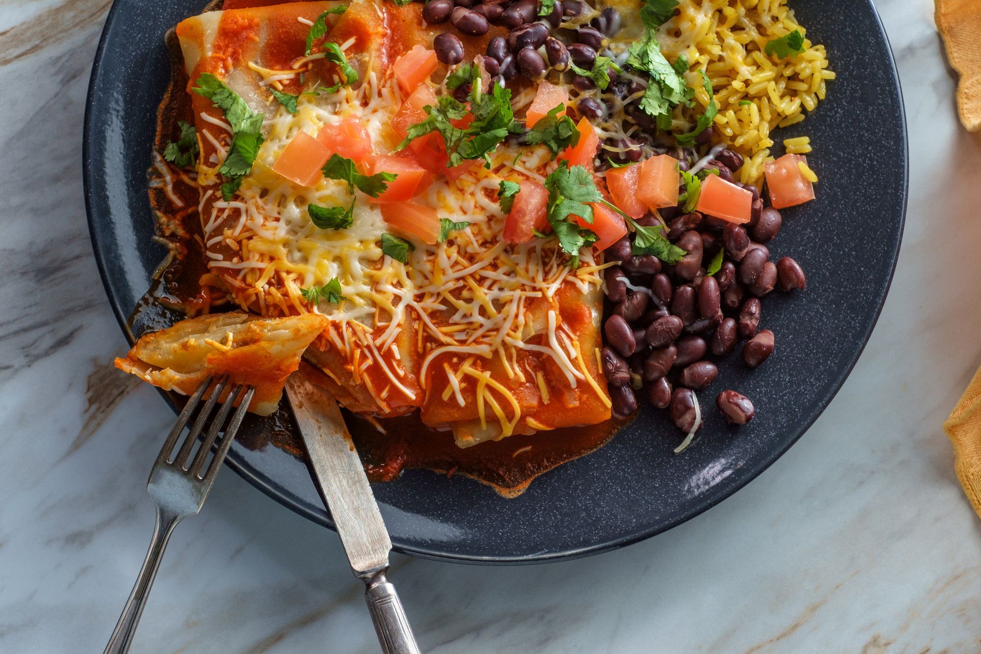 Enchiladas with melted cheese, tomato, cilantro, black beans, and yellow rice on a plate. Enchiladas with melted cheese, tomato, cilantro, black beans, and yellow rice on a plate.