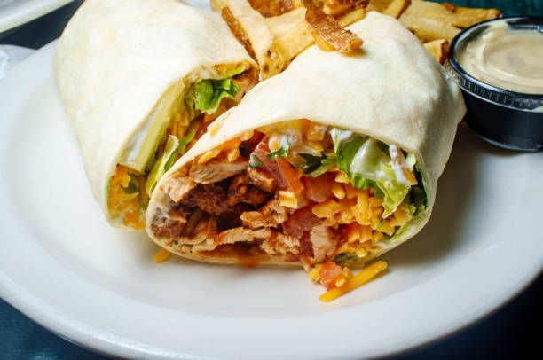 Chicken wrap cut in half with lettuce, cheese, and fries on a white plate.