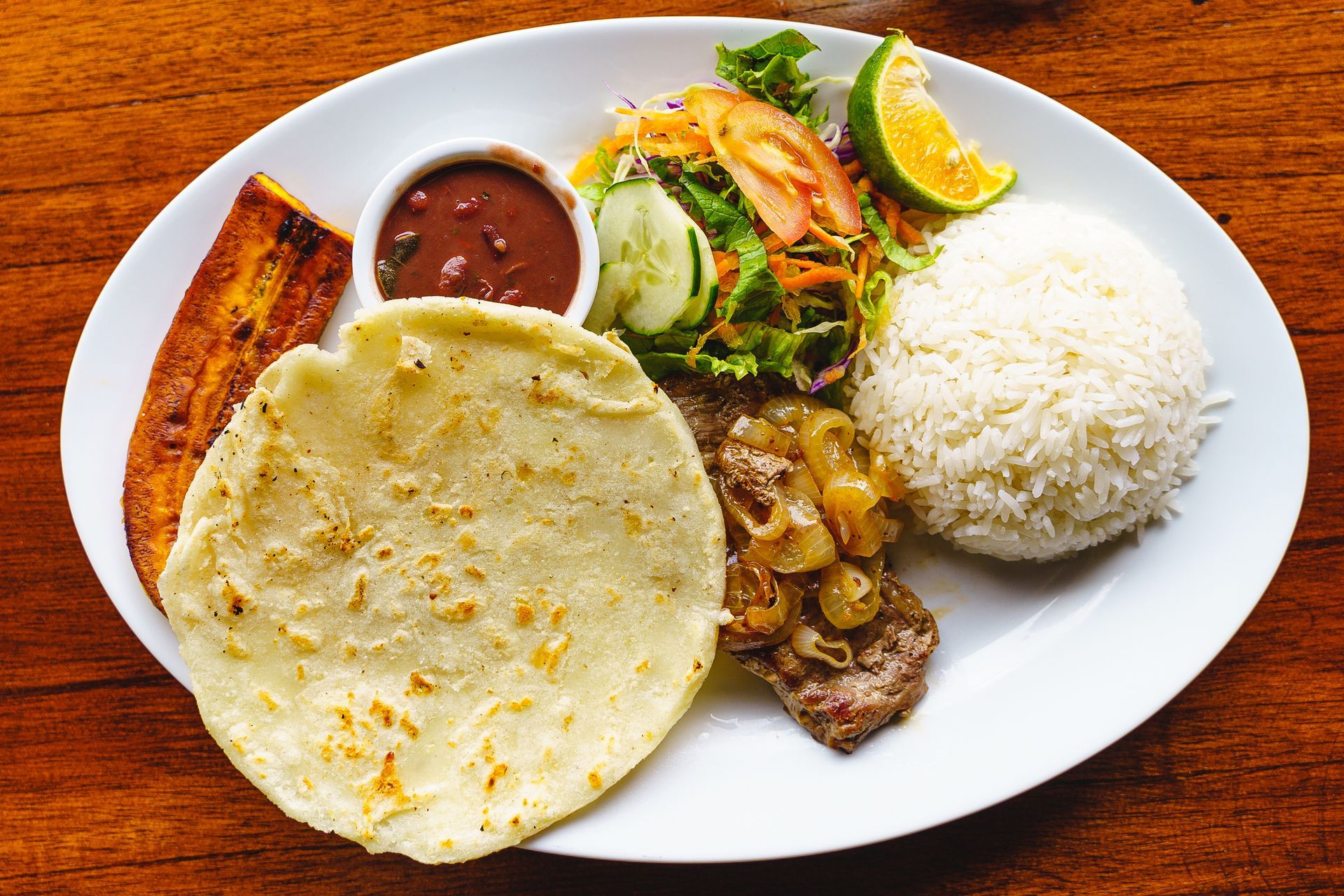 Plate of food with rice, beans, salad, meat, tortilla, and plantain, with a lime wedge. Plate of food with rice, beans, salad, meat, tortilla, and plantain, with a lime wedge.