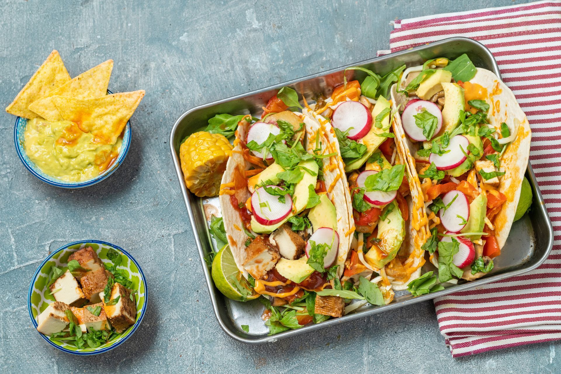 Tacos on tray with avocado, radishes, cilantro, and guacamole with chips and a side of ingredients. Tacos on tray with avocado, radishes, cilantro, and guacamole with chips and a side of ingredients.