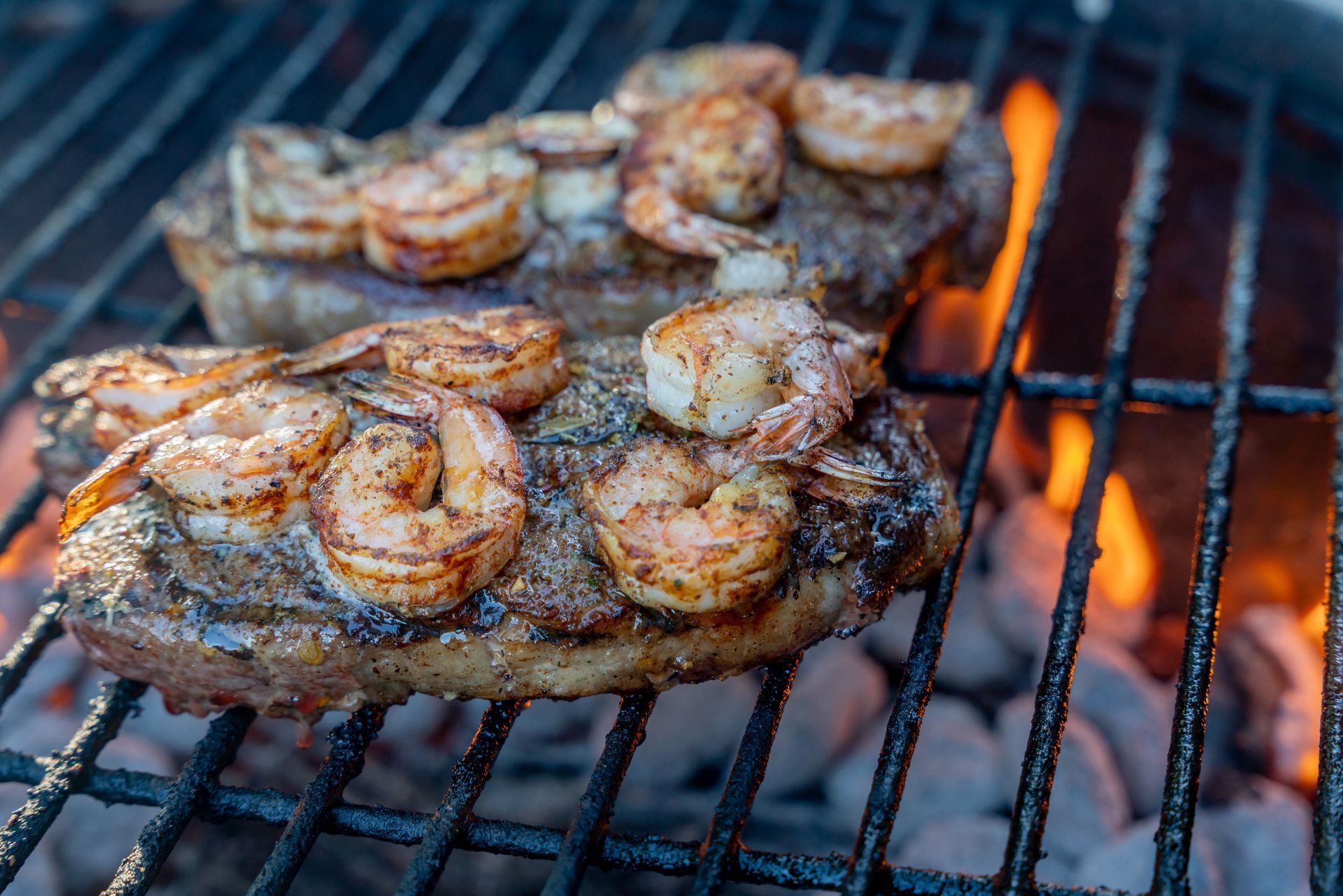 Steak and shrimp grilling on a barbecue, with flames visible. Steak and shrimp grilling on a barbecue, with flames visible.