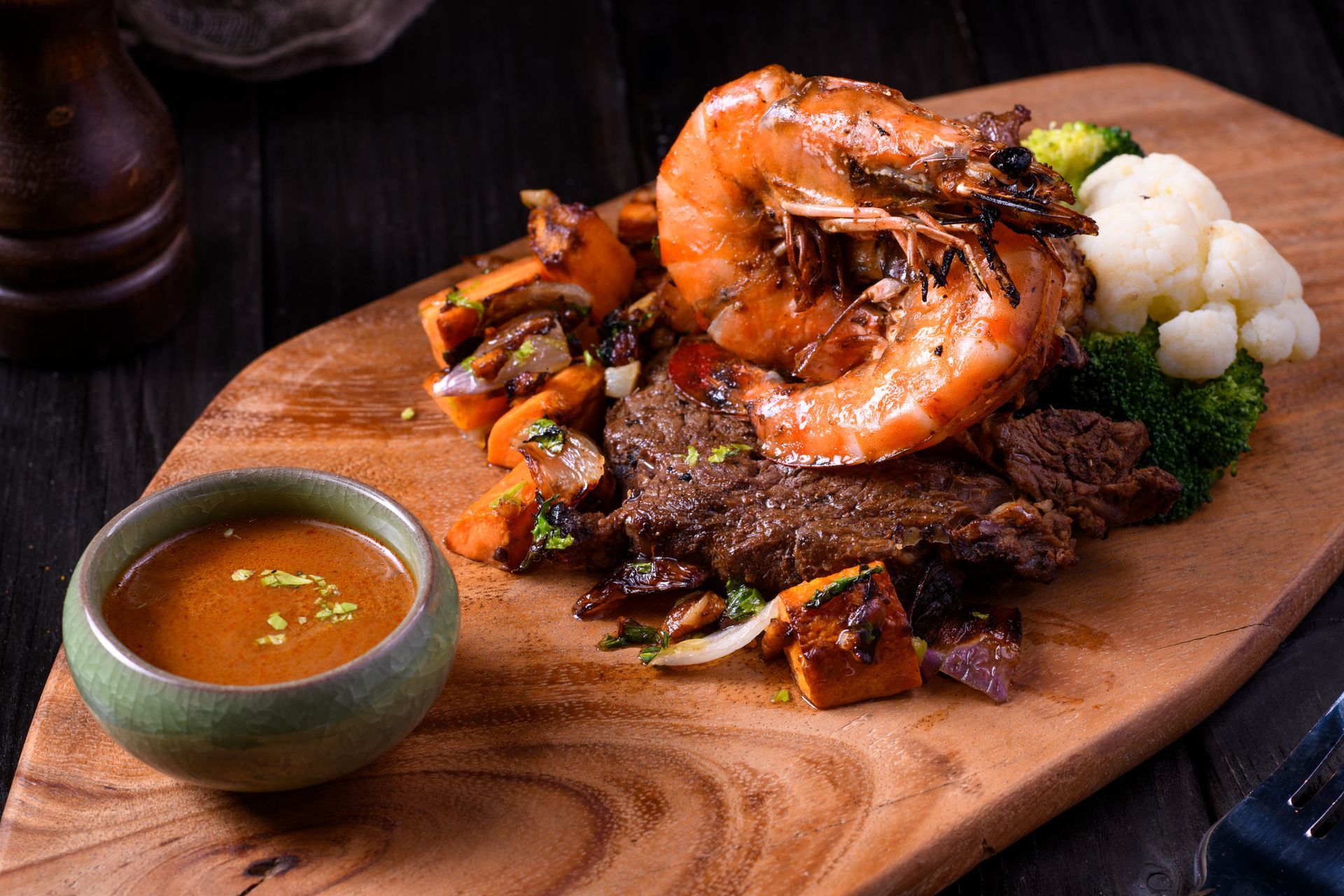 Grilled steak and shrimp with roasted vegetables and sauce on a wooden board. Grilled steak and shrimp with roasted vegetables and sauce on a wooden board.