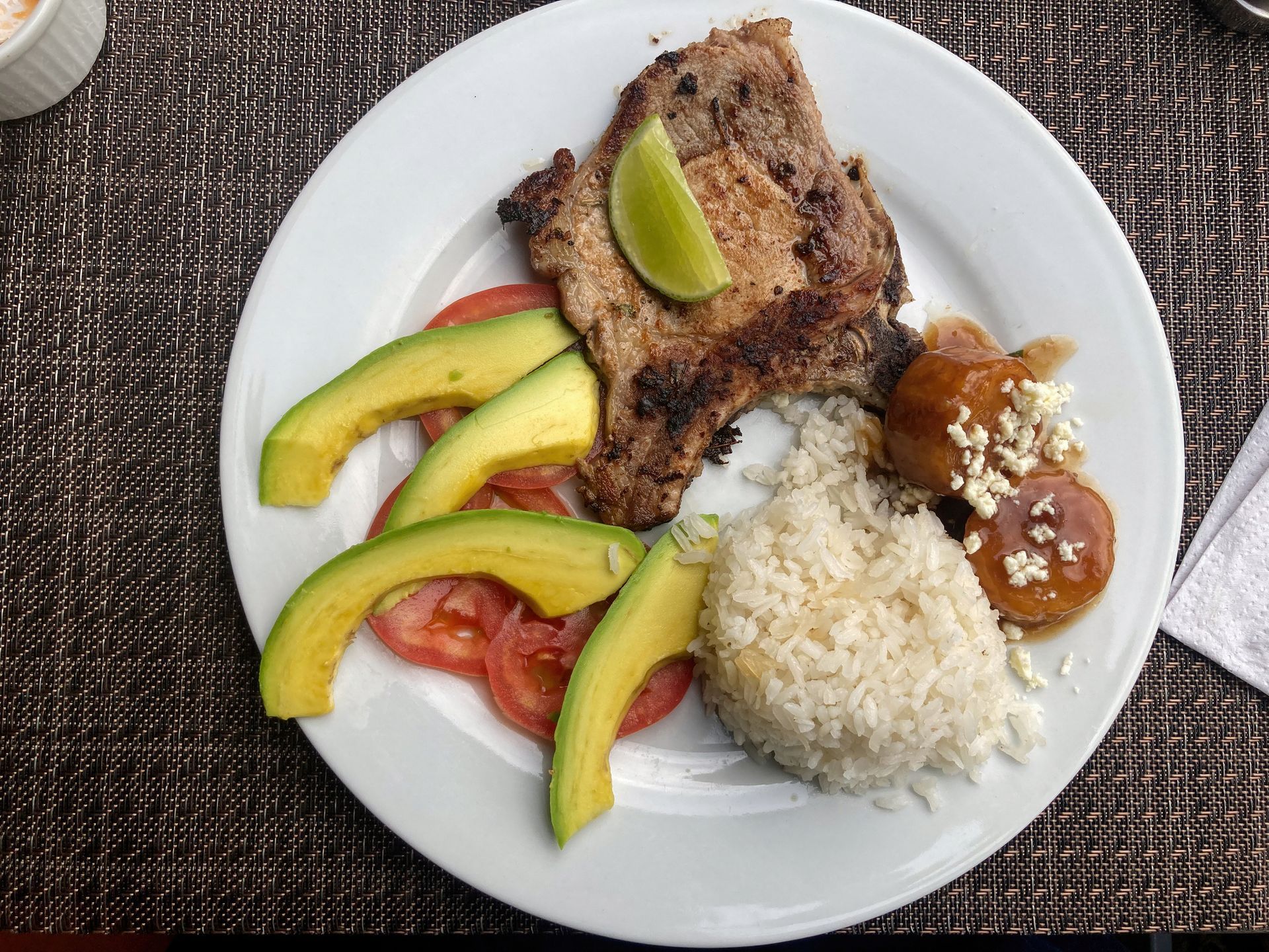 Plate of food: grilled pork chop with rice, avocado, tomatoes, sausage, and lime. Plate of food: grilled pork chop with rice, avocado, tomatoes, sausage, and lime.