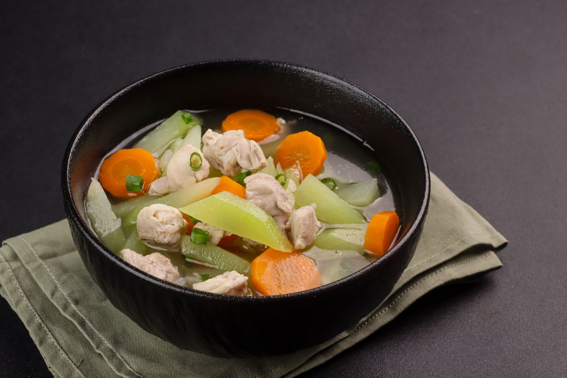 Soup with carrots, green vegetables, and chicken in a black bowl on a green napkin. Soup with carrots, green vegetables, and chicken in a black bowl on a green napkin.