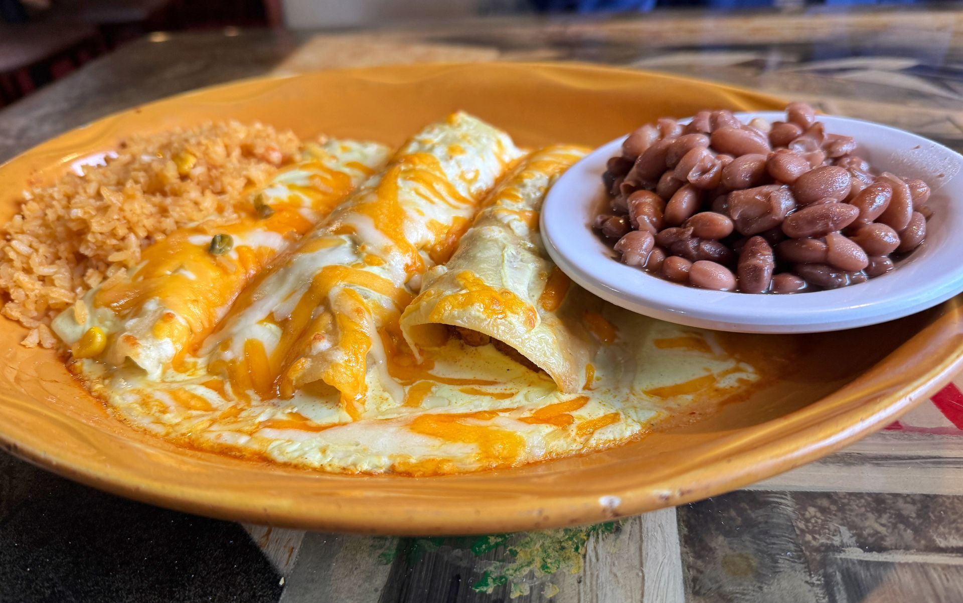 Enchiladas with cheese, rice, and beans on an orange plate. Enchiladas with cheese, rice, and beans on an orange plate.