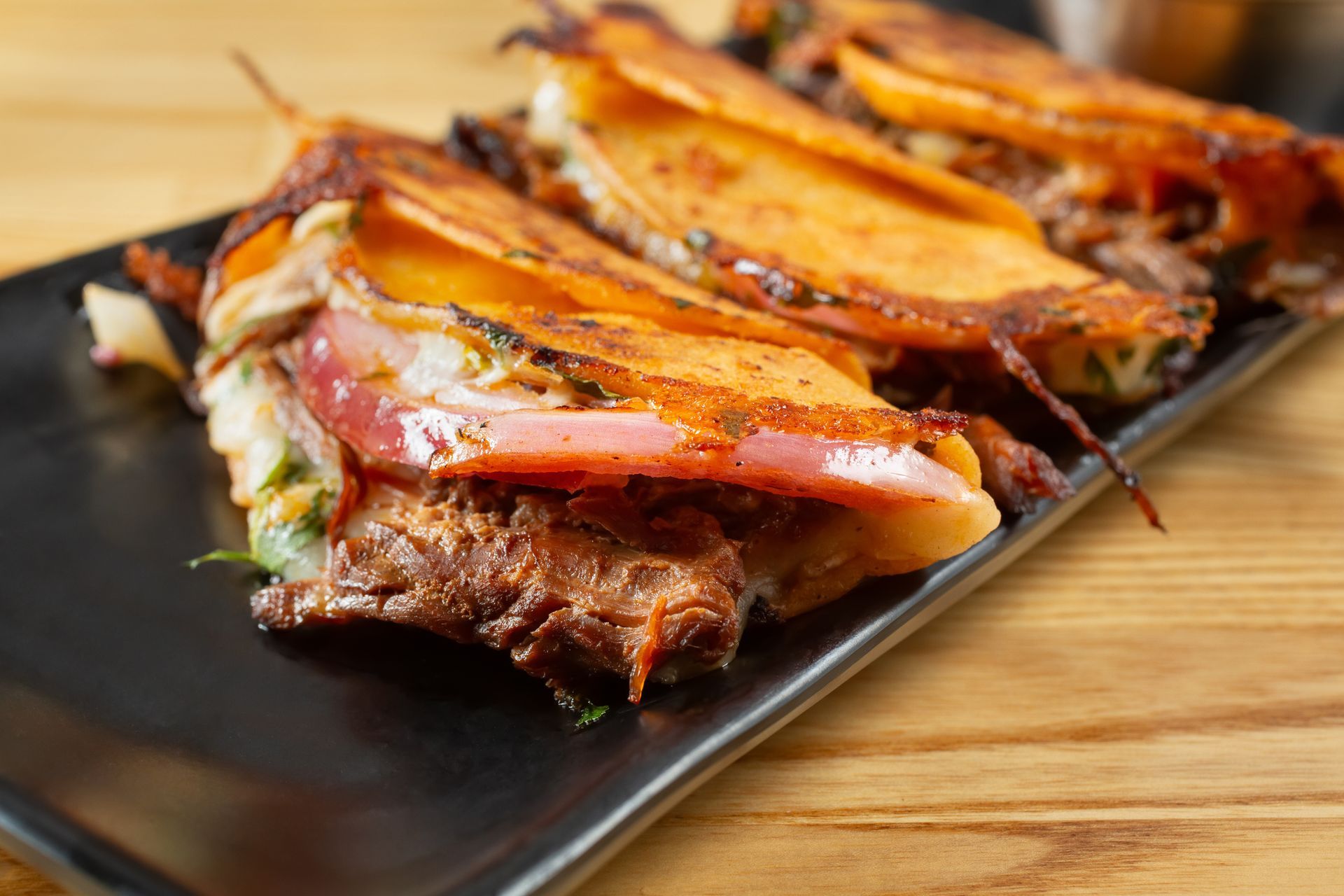 Birria tacos on a black plate, golden-brown tortillas filled with meat and cheese. Birria tacos on a black plate, golden-brown tortillas filled with meat and cheese.