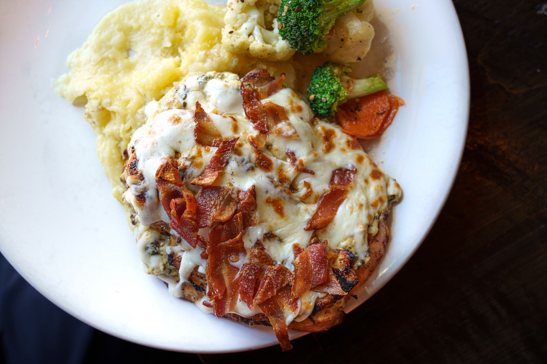 Chicken dish with melted cheese, bacon, and vegetables on a white plate. Chicken dish with melted cheese, bacon, and vegetables on a white plate.