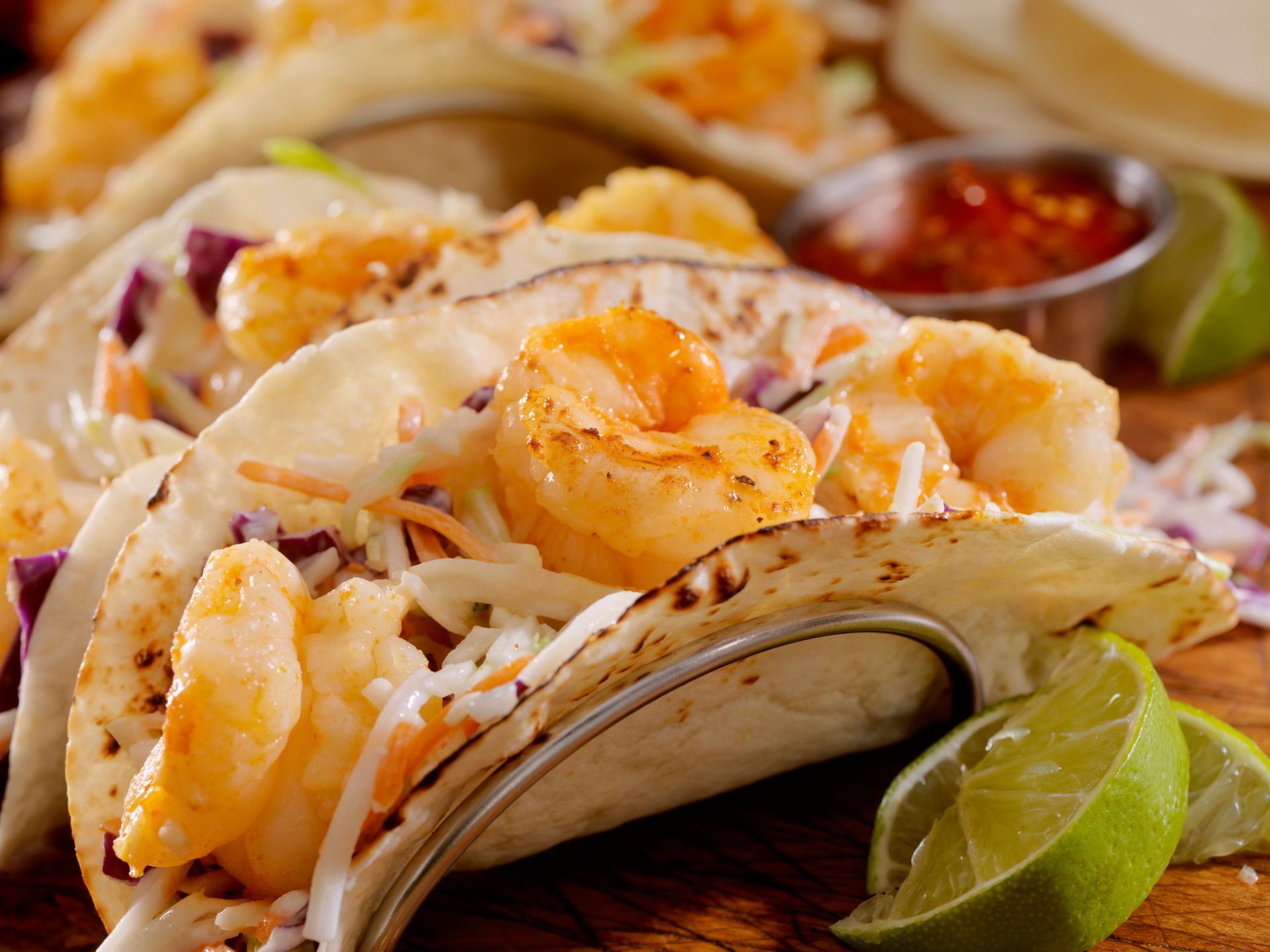 Shrimp tacos with slaw, lime wedges, and red sauce on a wooden surface. Shrimp tacos with slaw, lime wedges, and red sauce on a wooden surface.