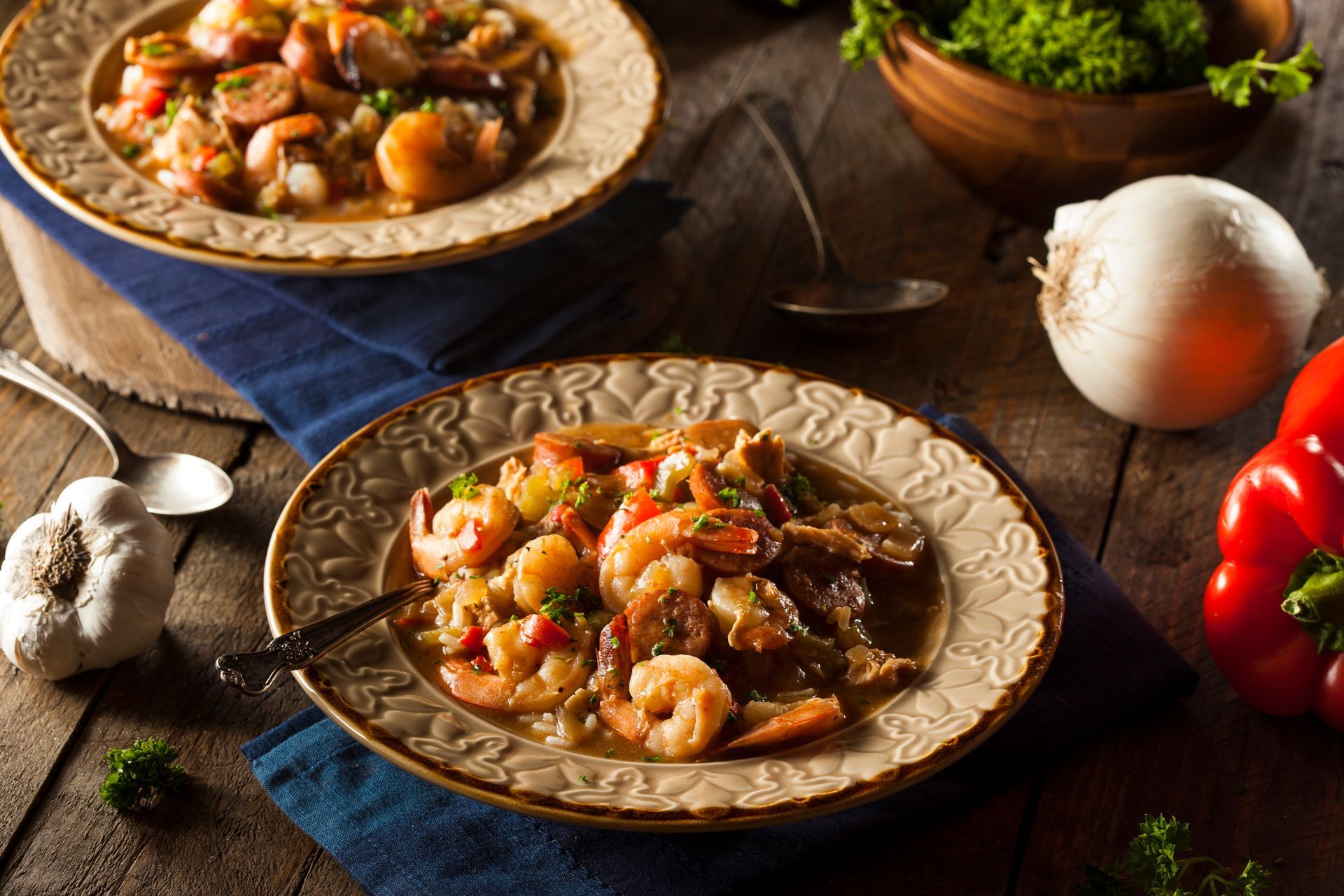 Two plates of shrimp and sausage gumbo, with vegetables, on a wooden table.