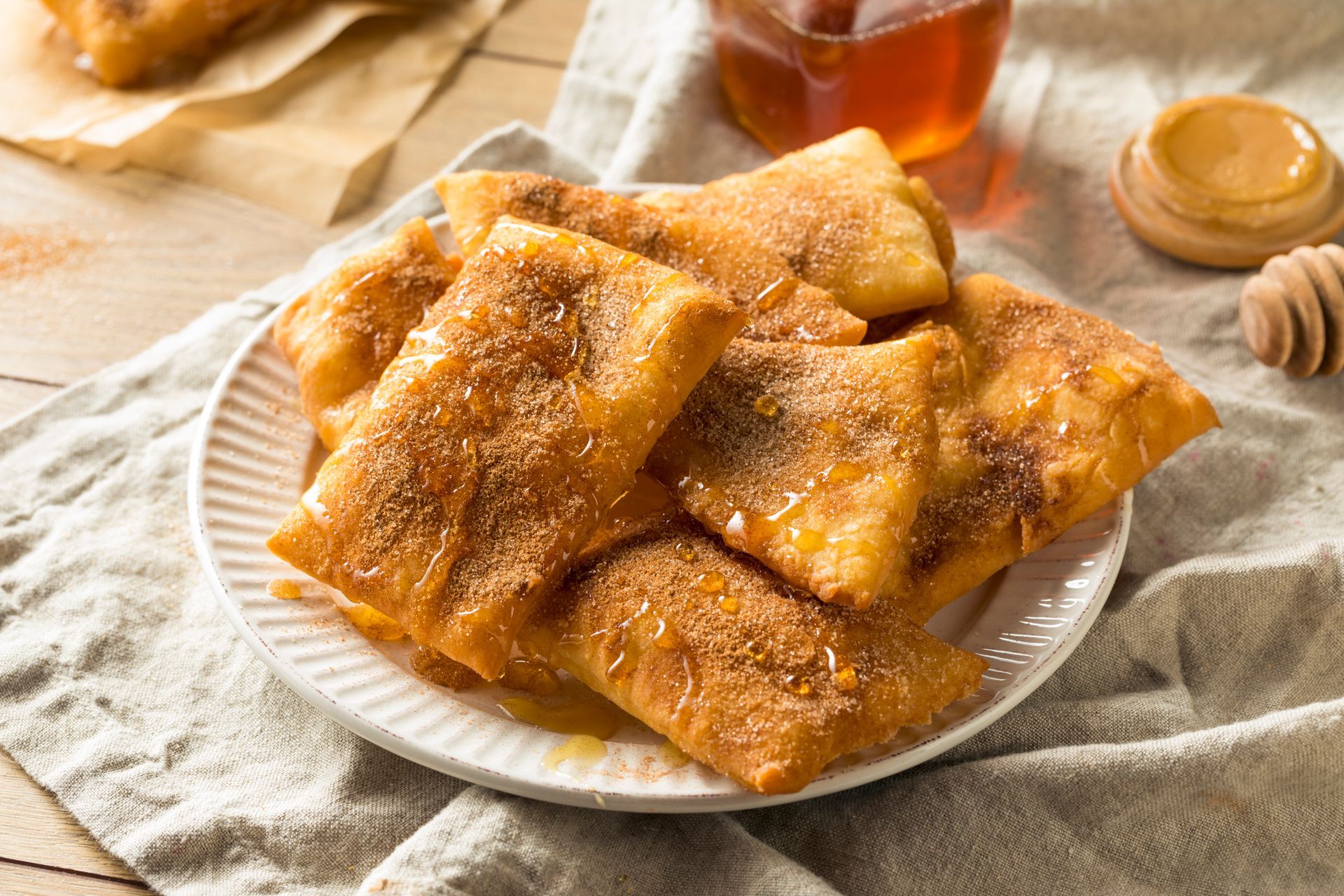 Plate of fried, golden pastries sprinkled with cinnamon-sugar, drizzled with honey.