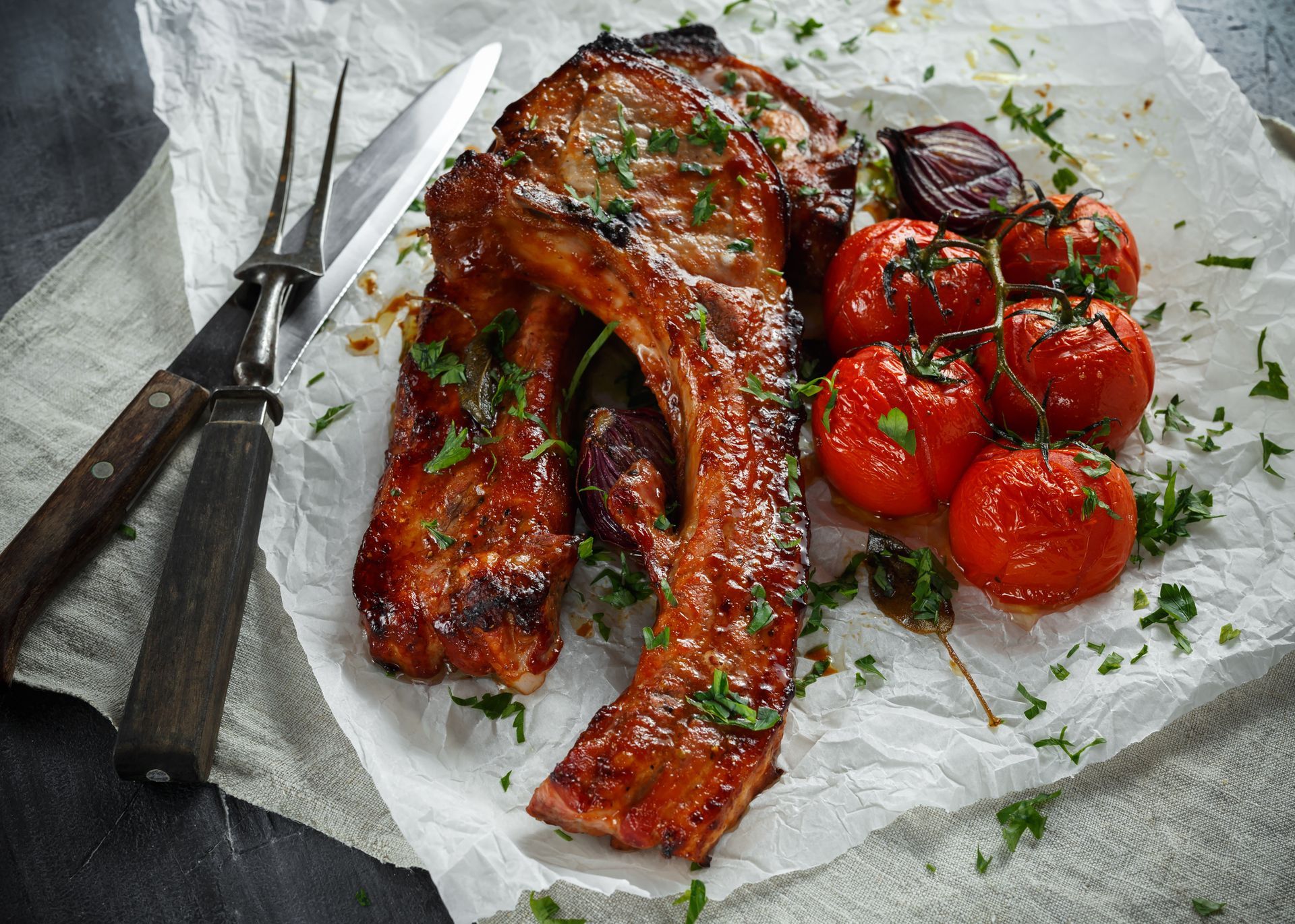 Grilled pork chop and roasted tomatoes on parchment paper.