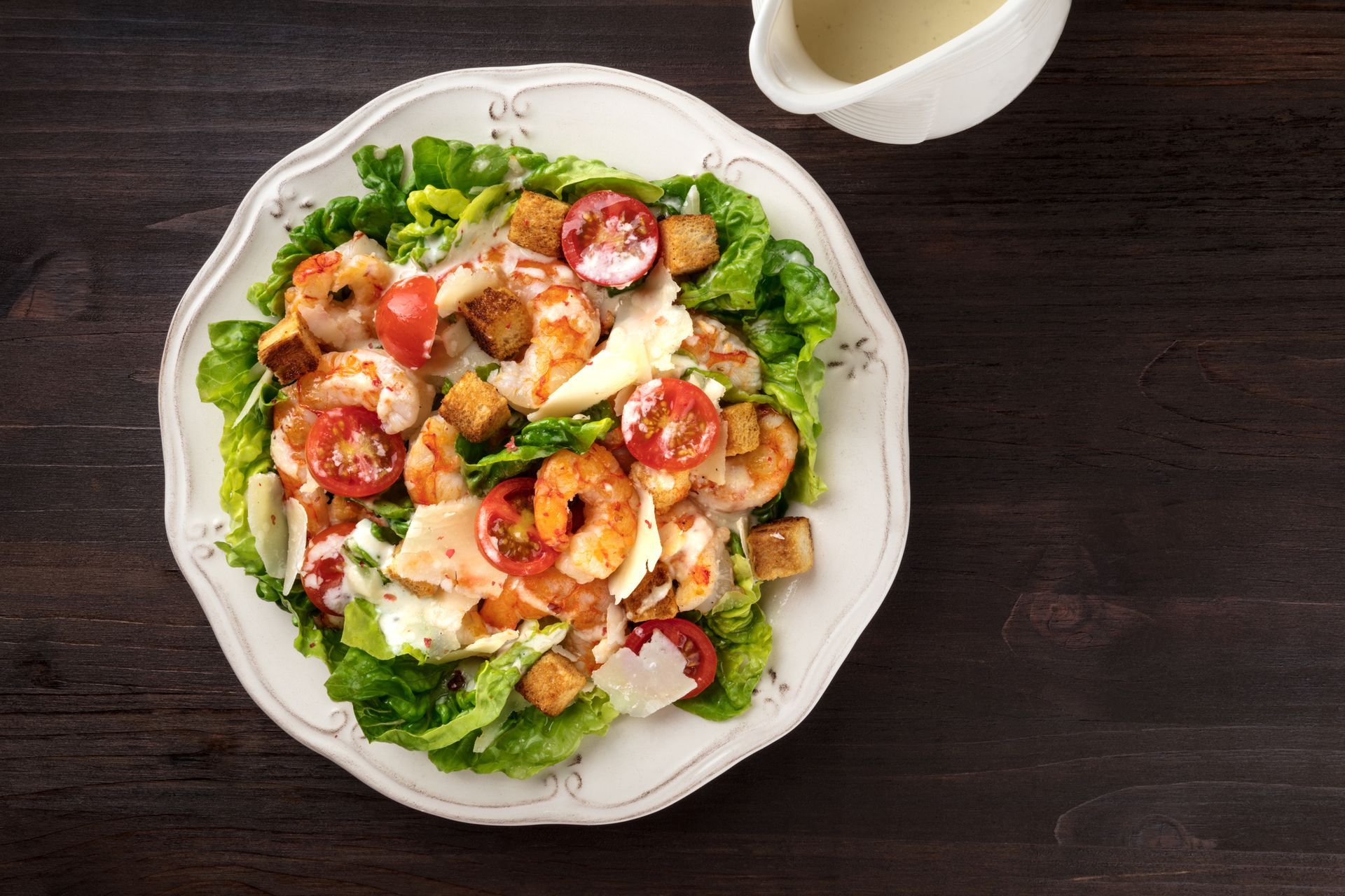 Shrimp Caesar salad on a white plate with dressing; dark wood background.