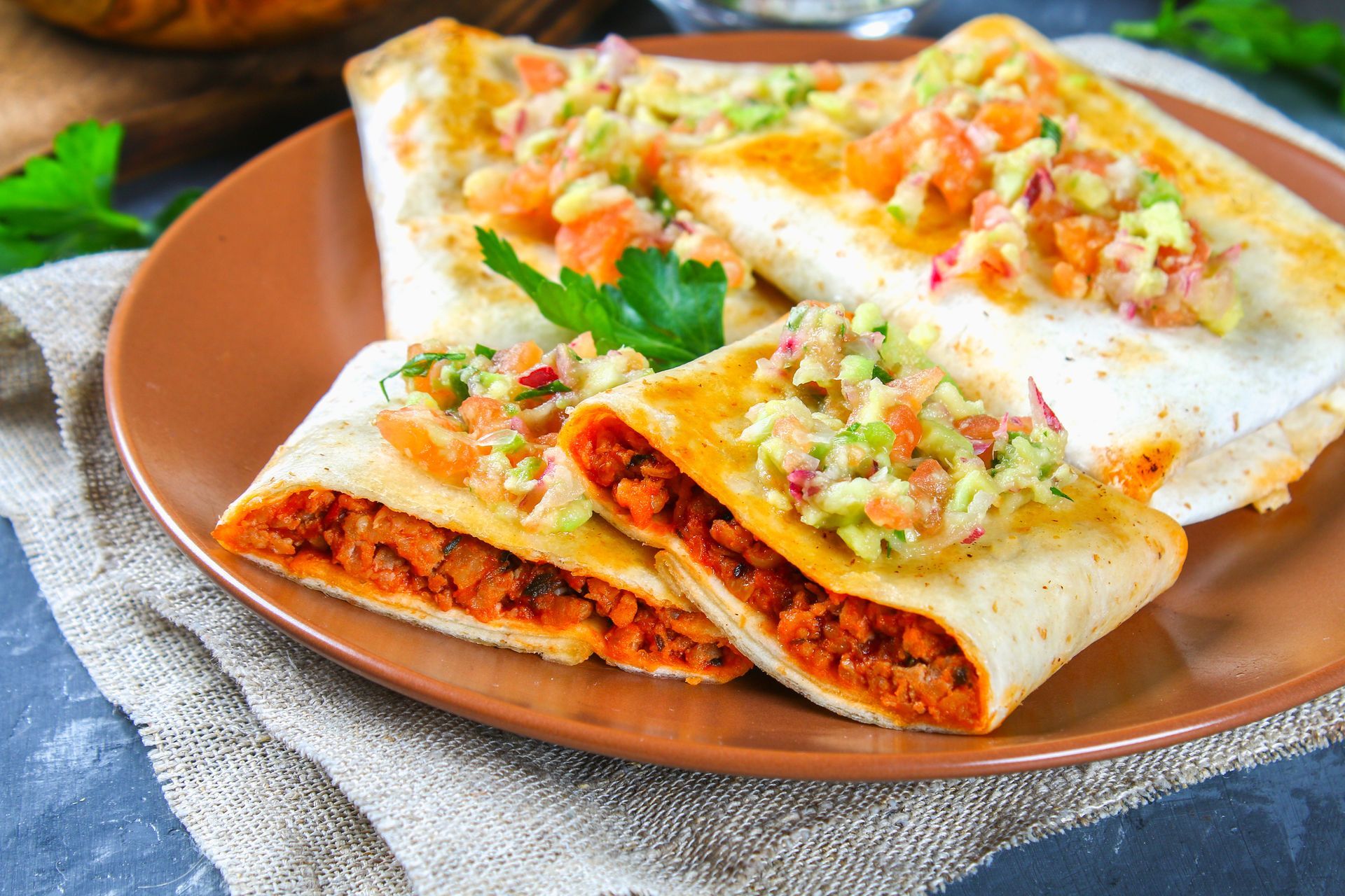 Burritos on a brown plate topped with salsa. One is cut open to show the filling.