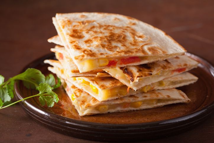 Stack of sliced quesadillas with corn and cheese on a brown plate, garnished with cilantro.