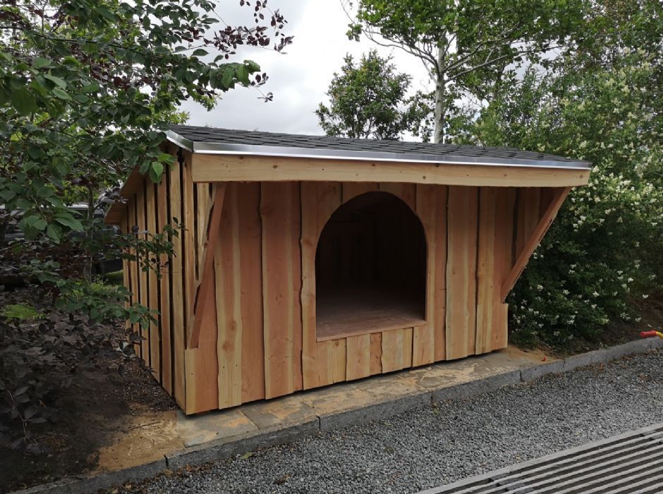 Et hundehus i træ sidder på siden af en grusvej.