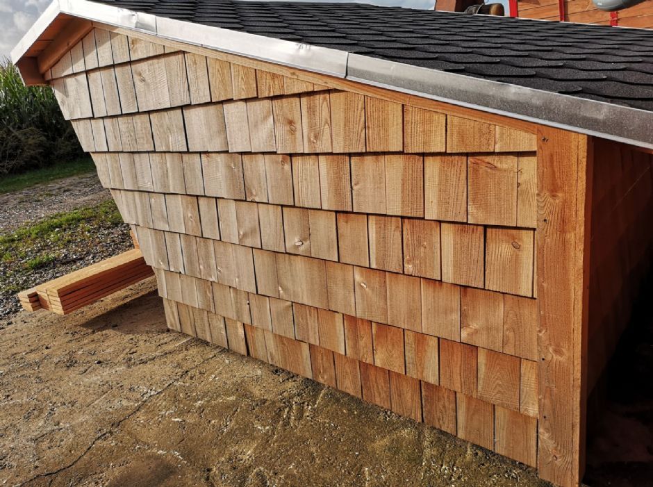 Et træskur med sort tag sidder på toppen af en jordmark.