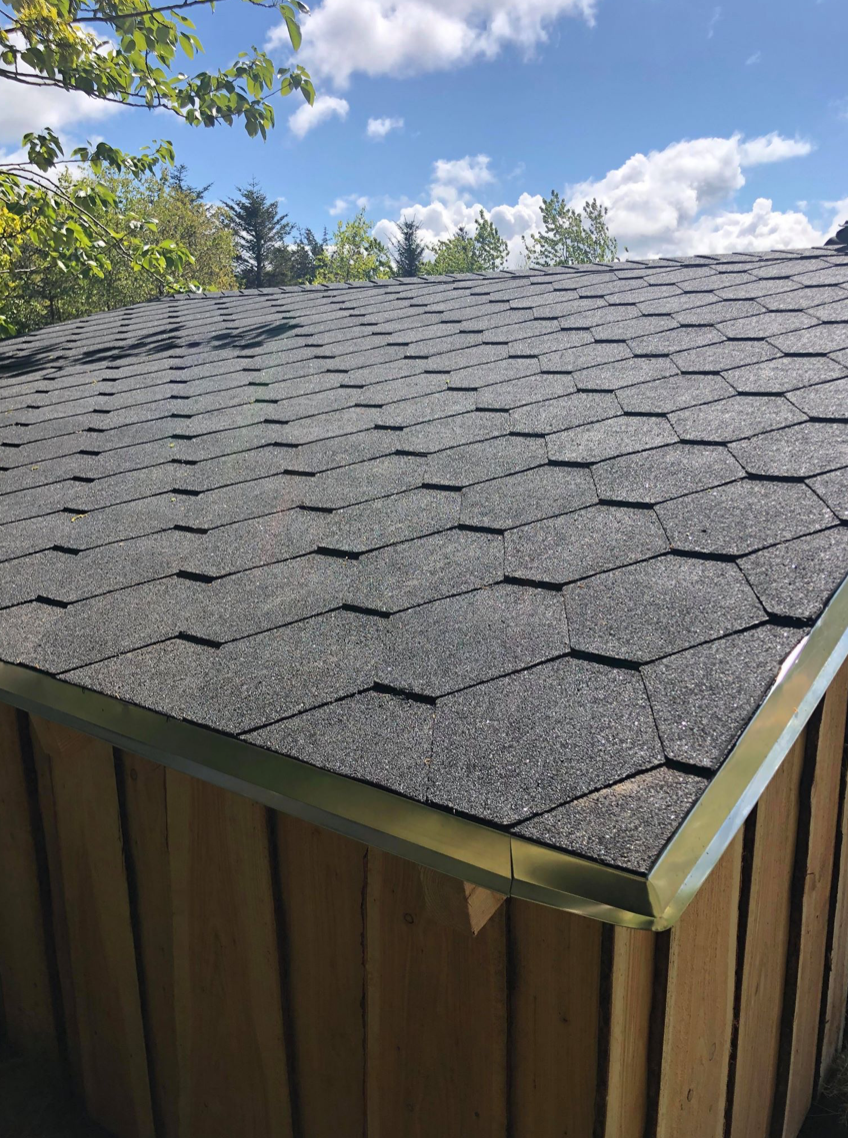 Et træskur med sort tag og en blå himmel i baggrunden.