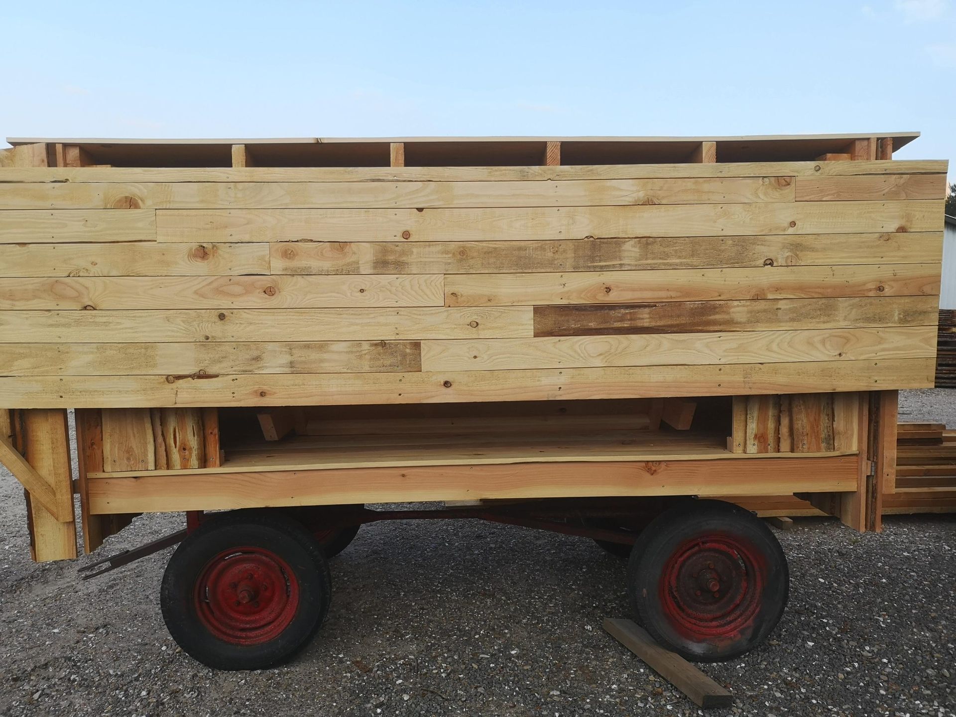 En trævogn med røde hjul sidder på grus.