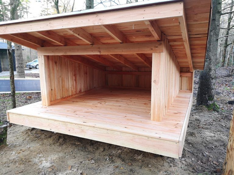 Et hundehus i træ sidder midt i en skov.