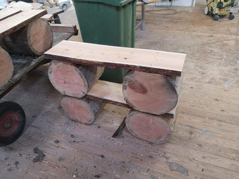 En træbænk lavet af bjælker sidder på et trægulv