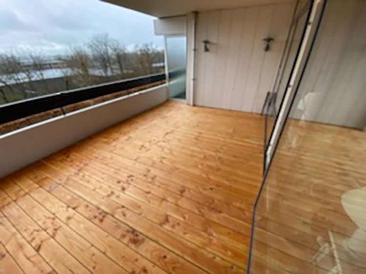 En balkon med træterrasse og glasskydedøre.